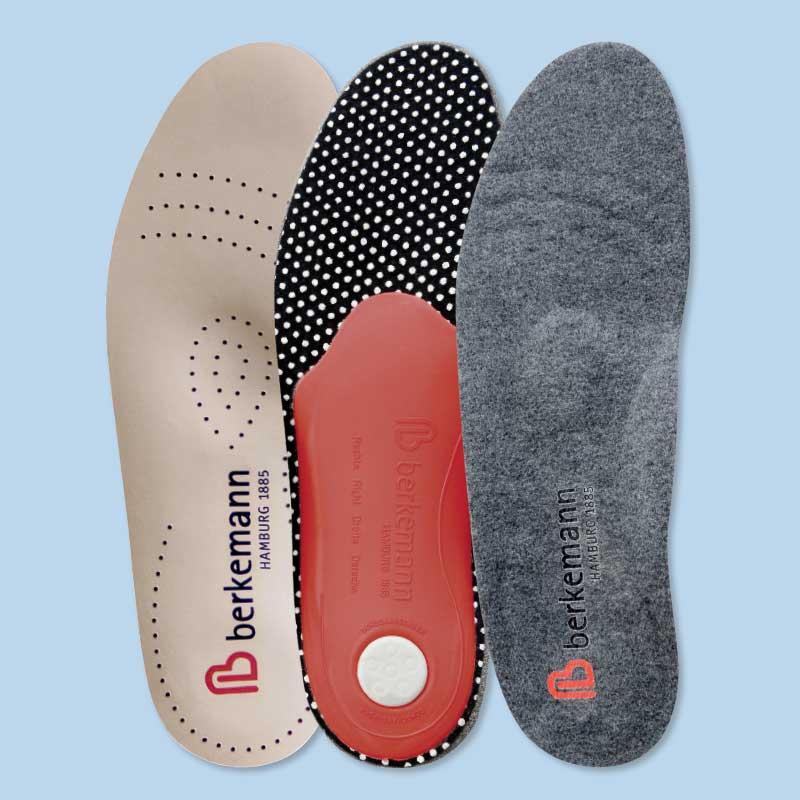 Drei verschiedene Berkemann-Einlegesohlen nebeneinander auf hellblauem Hintergrund: beige mit Perforation, schwarz mit weißen Punkten und rotem Fersenpolster sowie grau aus Filz.