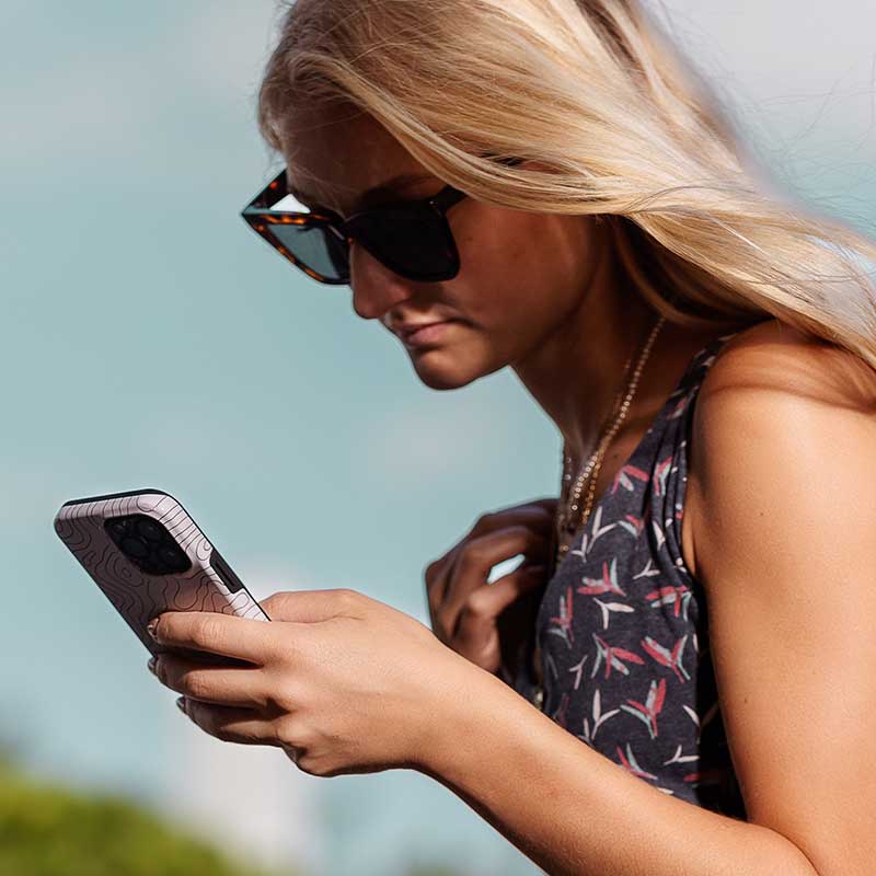 Frau mit Sonnenbrille schaut konzentriert auf ihr Smartphone, im Freien bei sonnigem Wetter.