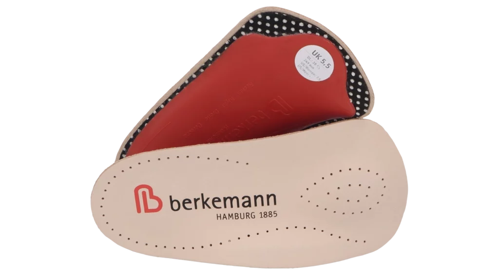 Berkemann-Einlegesohle Berkodur Fußbrücke halb, seitlich übereinanderliegend gezeigt. Oberseite aus beigem, fein perforiertem Leder mit rotem Berkemann-Logo, Unterseite rot mit schwarzer Punktstruktur und Fersenpolster.