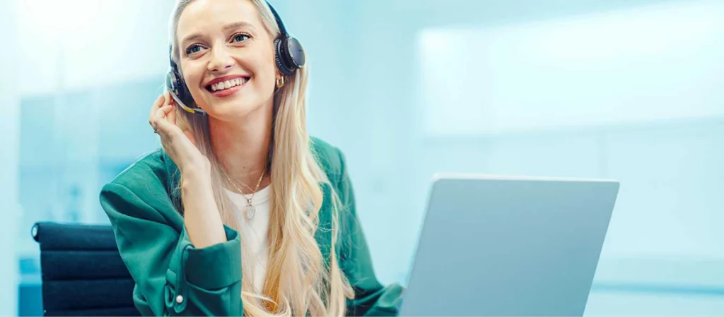 Frau mit Headset sitzt lächelnd am Laptop – Symbolbild für freundlichen Kundenservice.