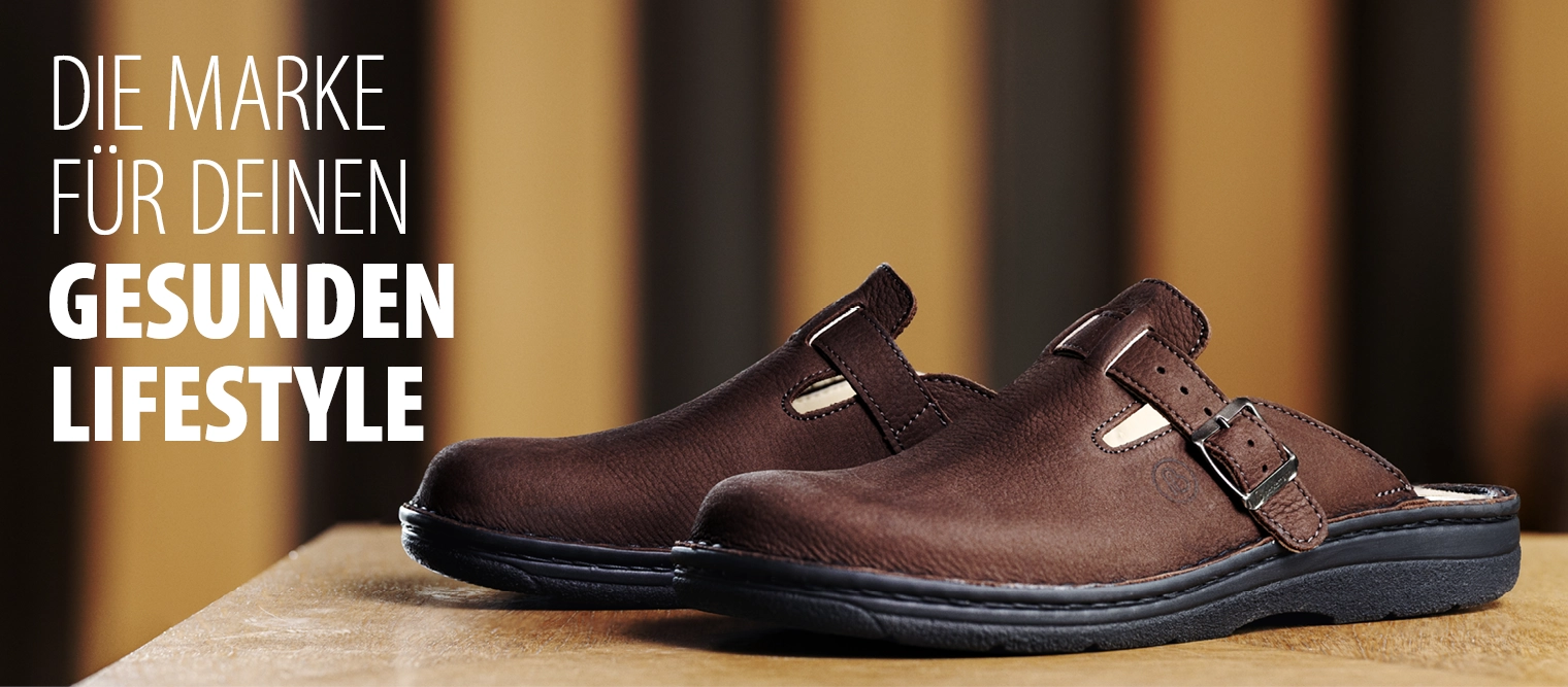 Brauner Lederclog von Berkemann, Modell Max, mit verstellbarem Riemen; unscharfer Innenraum im Hintergrund.