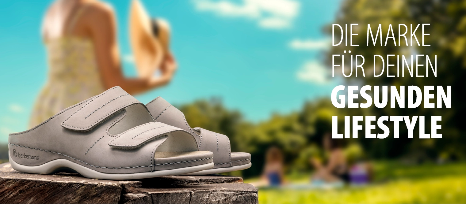 Graue Damen-Pantolette von Berkemann, Modell Daria, mit zwei Klettverschlüssen; im Hintergrund unscharf Personen im Park.