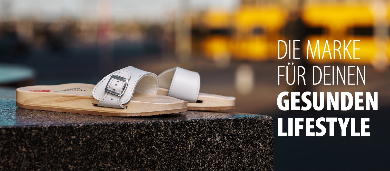 Weiße Berkemann Original-Sandale mit Holzsohle, aufgestellt im Außenbereich; Seitenansicht.