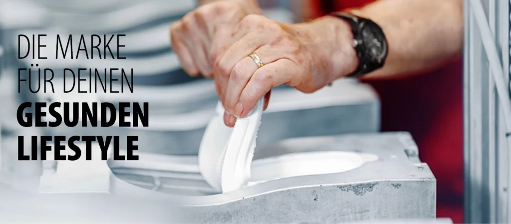 Hand zieht eine weiße Schuhsohle aus der metallischen Gussform einer Produktionslinie.