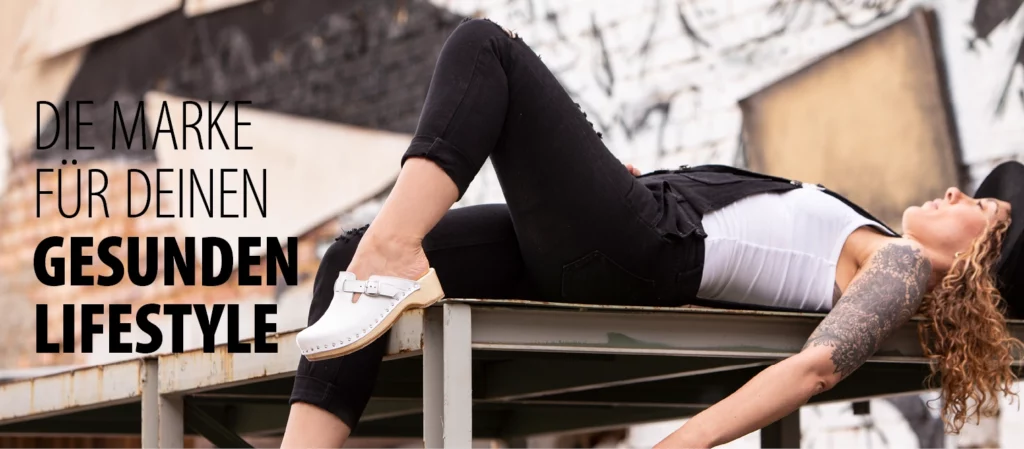 Junge Frau in weißem Top und schwarzer Hose liegt entspannt auf einer Metallplattform und trägt weiße Berkemann-Toeffler.