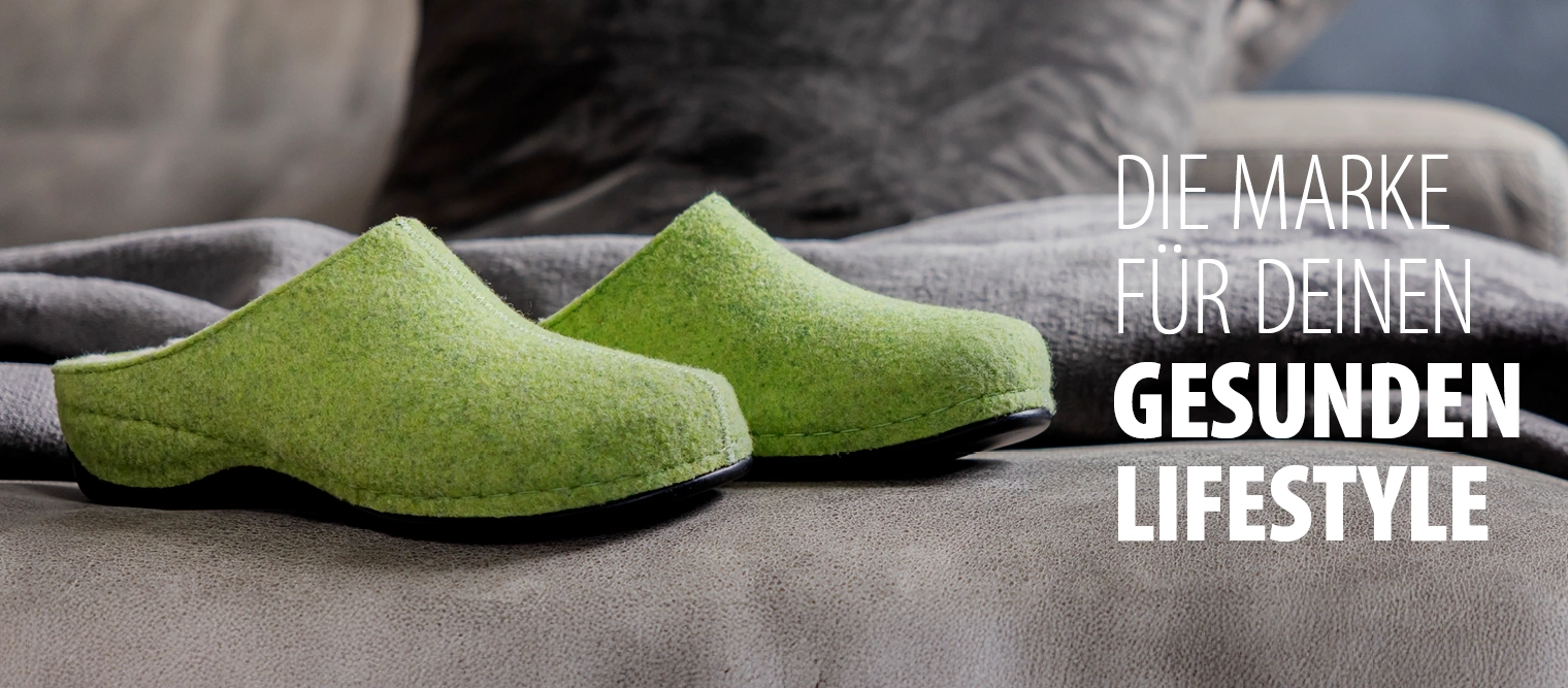 Hellgrüne Filzclogs von Berkemann, Modell Florina, auf grauem Sofa mit gefalteter Decke.