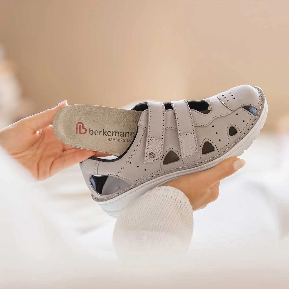 Person hält die graue Berkemann-Sandale Larena und zieht das herausnehmbare Wechselfußbett aus dem Schuh.