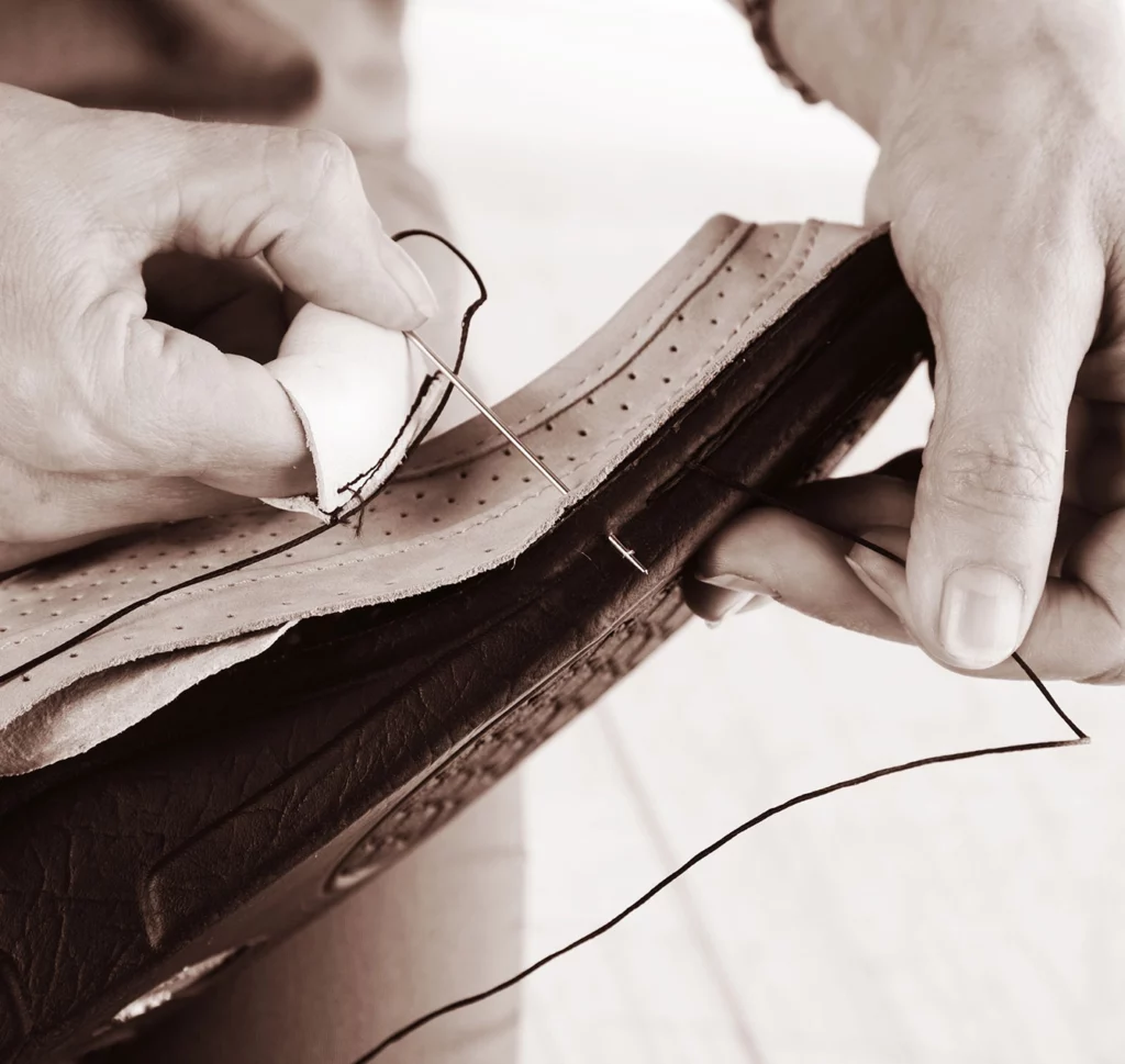 Hand näht mit Nadel und Faden ein Schuhteil aus Leder – Nahaufnahme traditioneller Handarbeit.