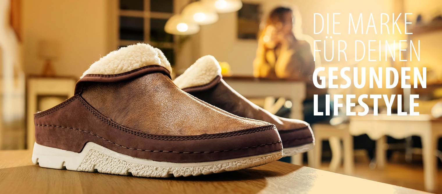 Berkemann-Hausschuh Remonda in whiskey Doubleface, in schräger Seitenansicht, in einer heimeliger, gelb-braunen Umgebung fotografiert