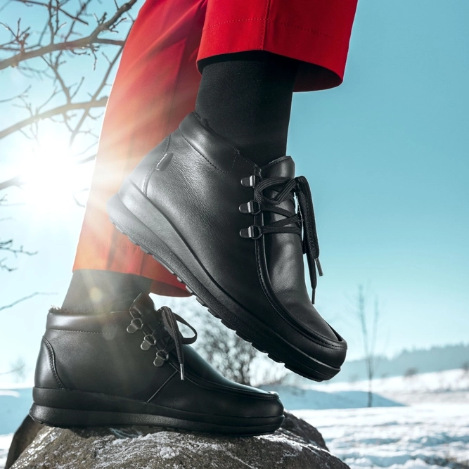 Stiefelette Sancia von Berkemann aus schwarzem Leder wird im winterlichen Außenbereich auf einem Stein getragen.